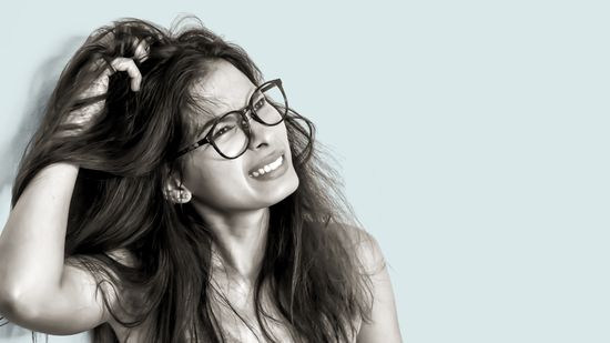 Woman with glasses showing discomfort while scratching an itchy, irritated scalp against a white background.
